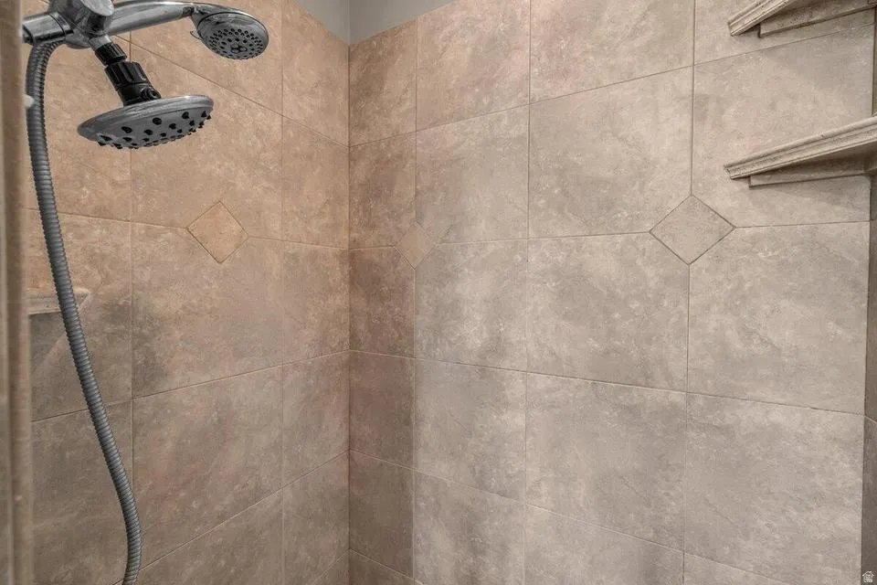 Tiled shower enclosure featuring a multi-function showerhead with a handheld sprayer, decorative diamond-patterned accent tiles, and built-in shelving