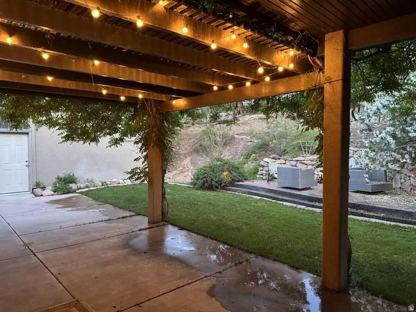Covered patio with string lighting, concrete flooring, and an adjacent manicured lawn