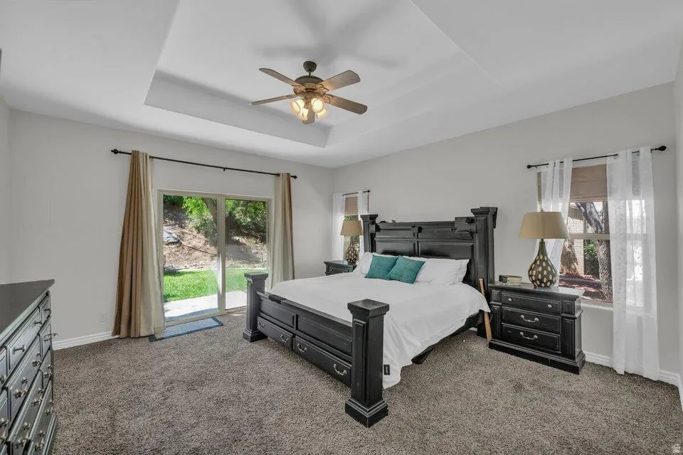 Recessed tray ceiling with ceiling fan, dual windows, and sliding glass door providing exterior access