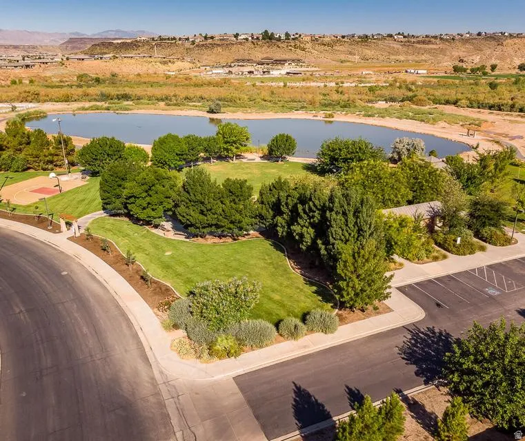 Expansive park area featuring a central pond, manicured green spaces, mature trees, a basketball court, and paved walkways