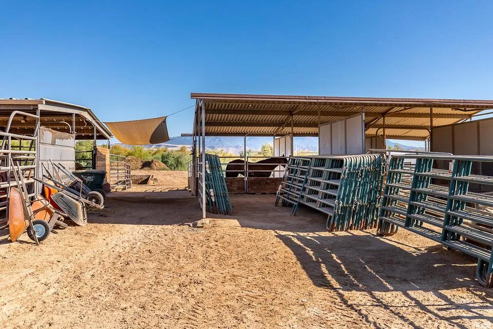 Outdoor equestrian facilities featuring covered stalls with metal roofing, multiple metal panel corrals, and a dirt ground surface