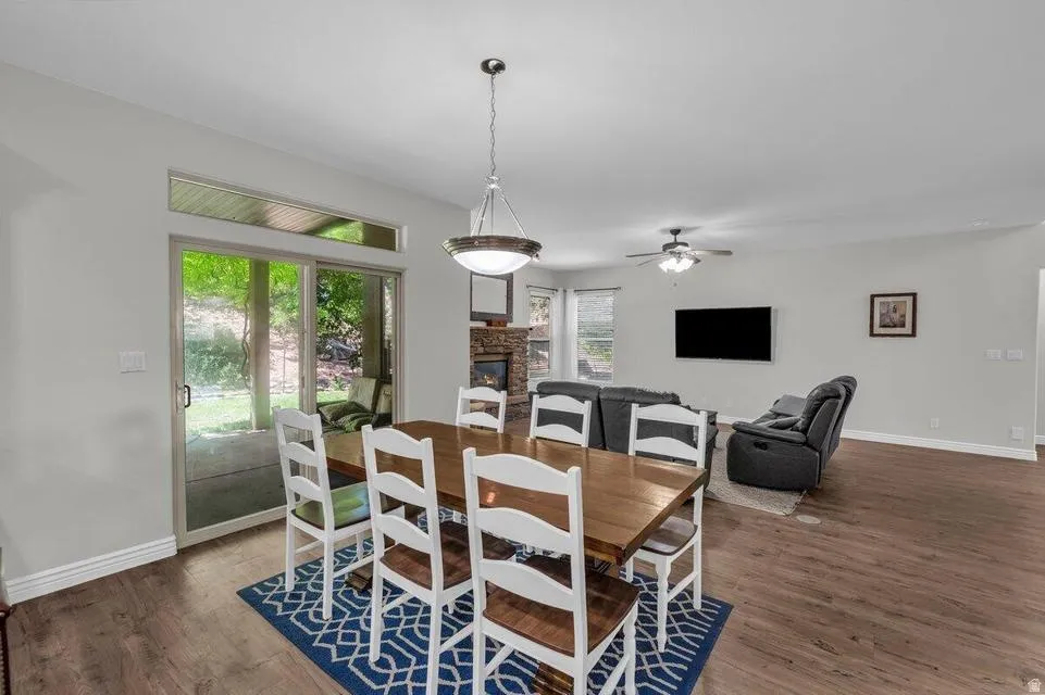 Open-concept living space featuring wood-finish flooring, a stone-surround fireplace, and a ceiling fan