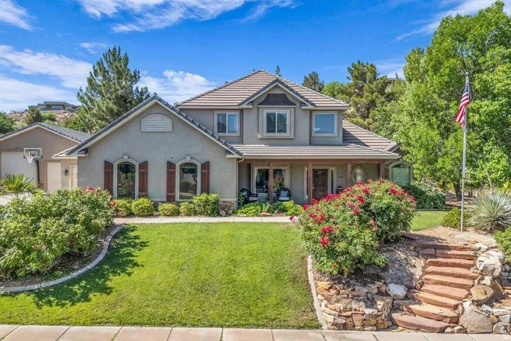 Stucco exterior residence featuring a covered front porch with dark wood pillars, arched windows with dark shutters, and a multi-level tile roof