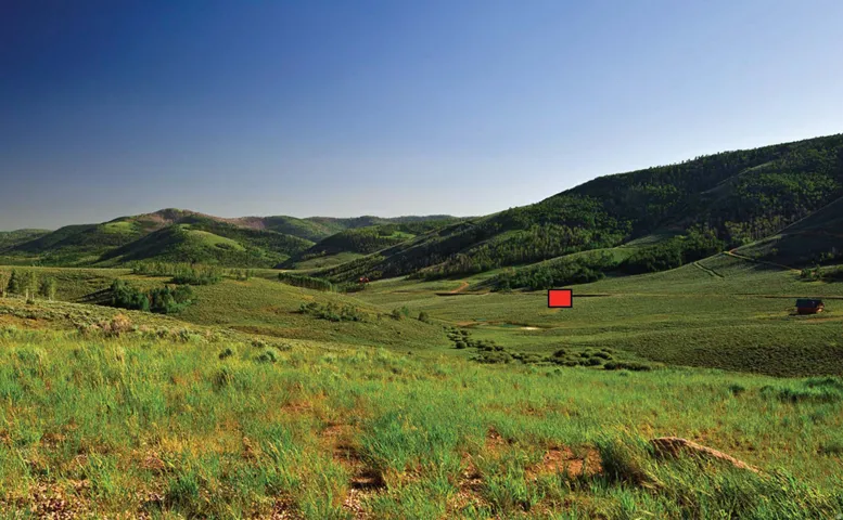 Expansive green hills with scattered trees, a distant rustic cabin, and a clear blue sky