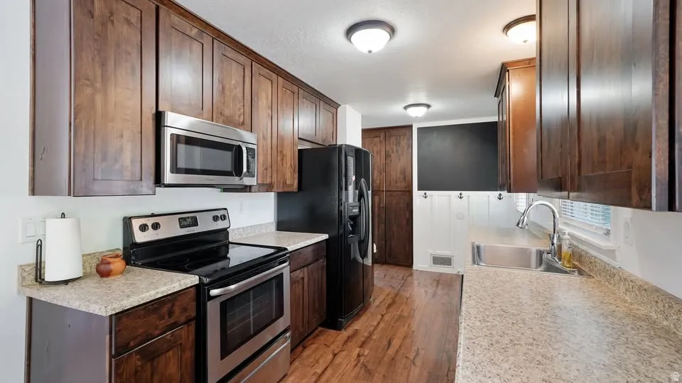 Kitchen featuring wood-finish cabinetry, stainless steel appliances, speckled countertops, and wood-finish flooring