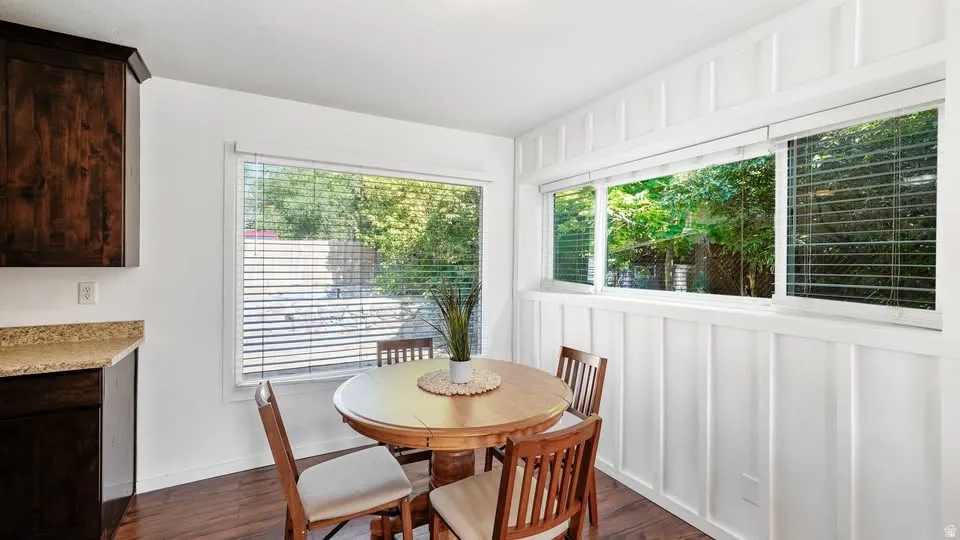 Dining area featuring a wall of windows, white board and batten paneling, dark wood-finish flooring, and dark wood cabinetry with a speckled countertop