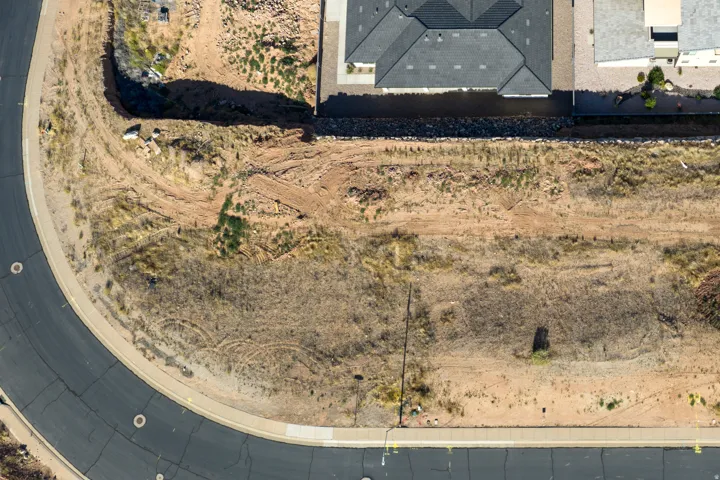 Curved paved road with concrete sidewalk bordering a vacant lot