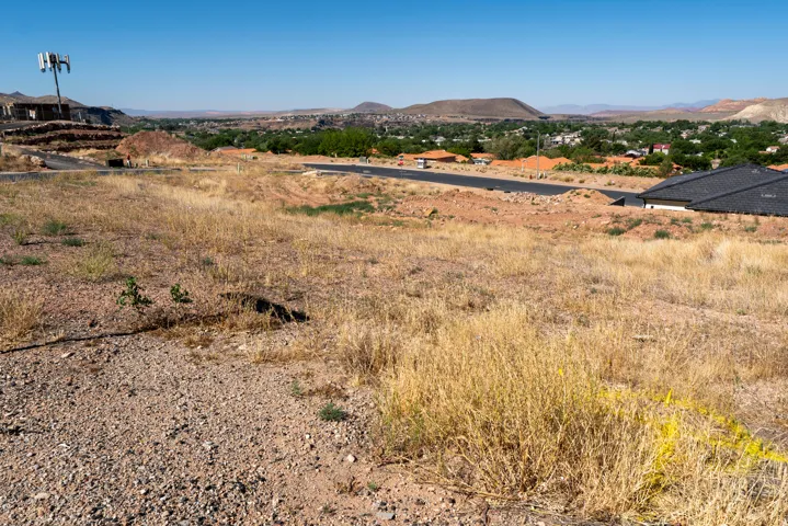 Expansive undeveloped land featuring a cleared building site, established road access, and distant residential areas