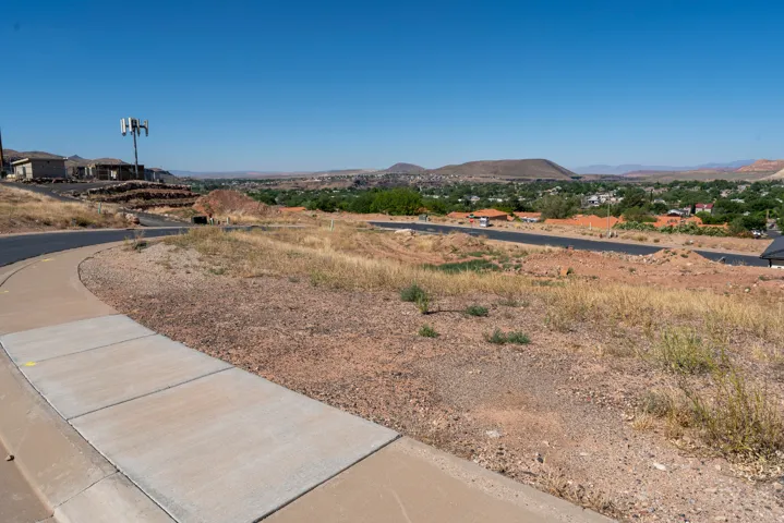 Expansive undeveloped lot featuring a paved road, concrete sidewalk, and natural desert landscaping