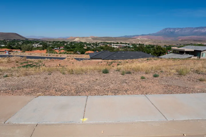 Expansive undeveloped lot featuring concrete sidewalk and pavement bordering the property