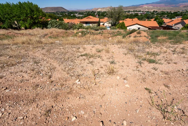 Arid terrain showcasing sparse vegetation and a distant residential area with terracotta-tiled roofs