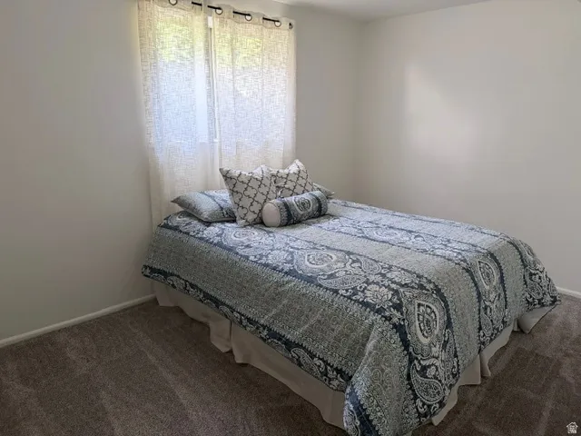 Bedroom with light gray carpeting, white walls, and a window featuring sheer curtains