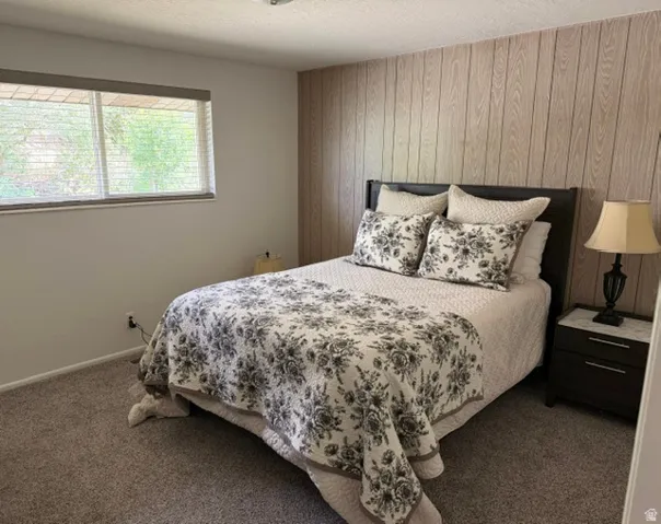 Bedroom featuring a full wall of vertical wood paneling, a large window with blinds, and neutral carpeting