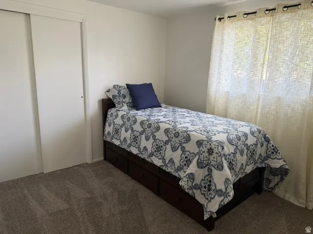 Carpeted room with a sliding closet door and a window featuring installed curtain rods