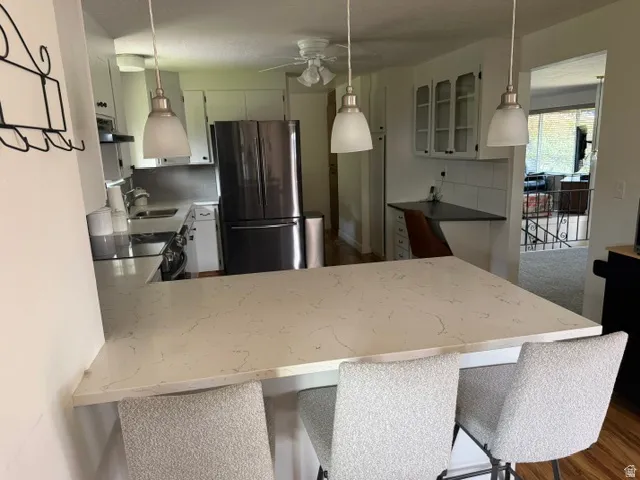Kitchen featuring a large light-toned countertop, white cabinetry with glass inserts, stainless steel appliances, and pendant lighting