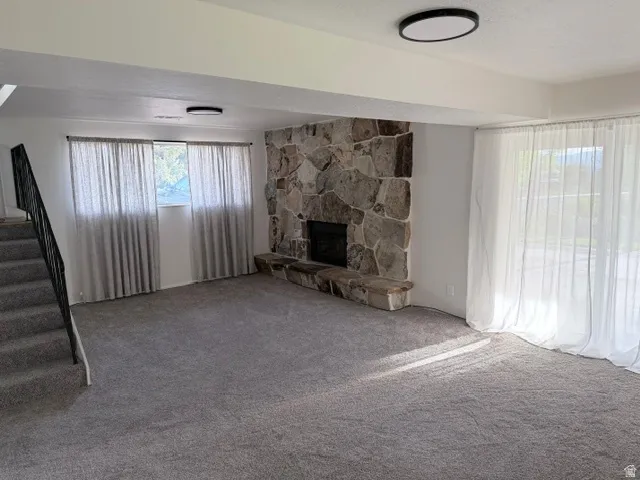 Spacious living area featuring a prominent stone fireplace, new gray carpet, and two flush-mount ceiling lights