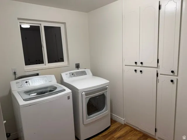 Laundry area featuring wood-finish flooring, white cabinetry with black hardware, and a sliding window