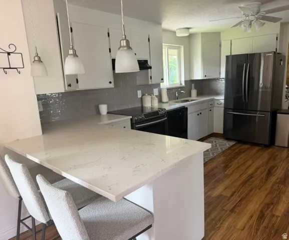 Kitchen featuring white shaker-style cabinetry, a large quartz-finish island with seating, pendant lighting, wood-finish flooring, and a stainless steel French door refrigerator