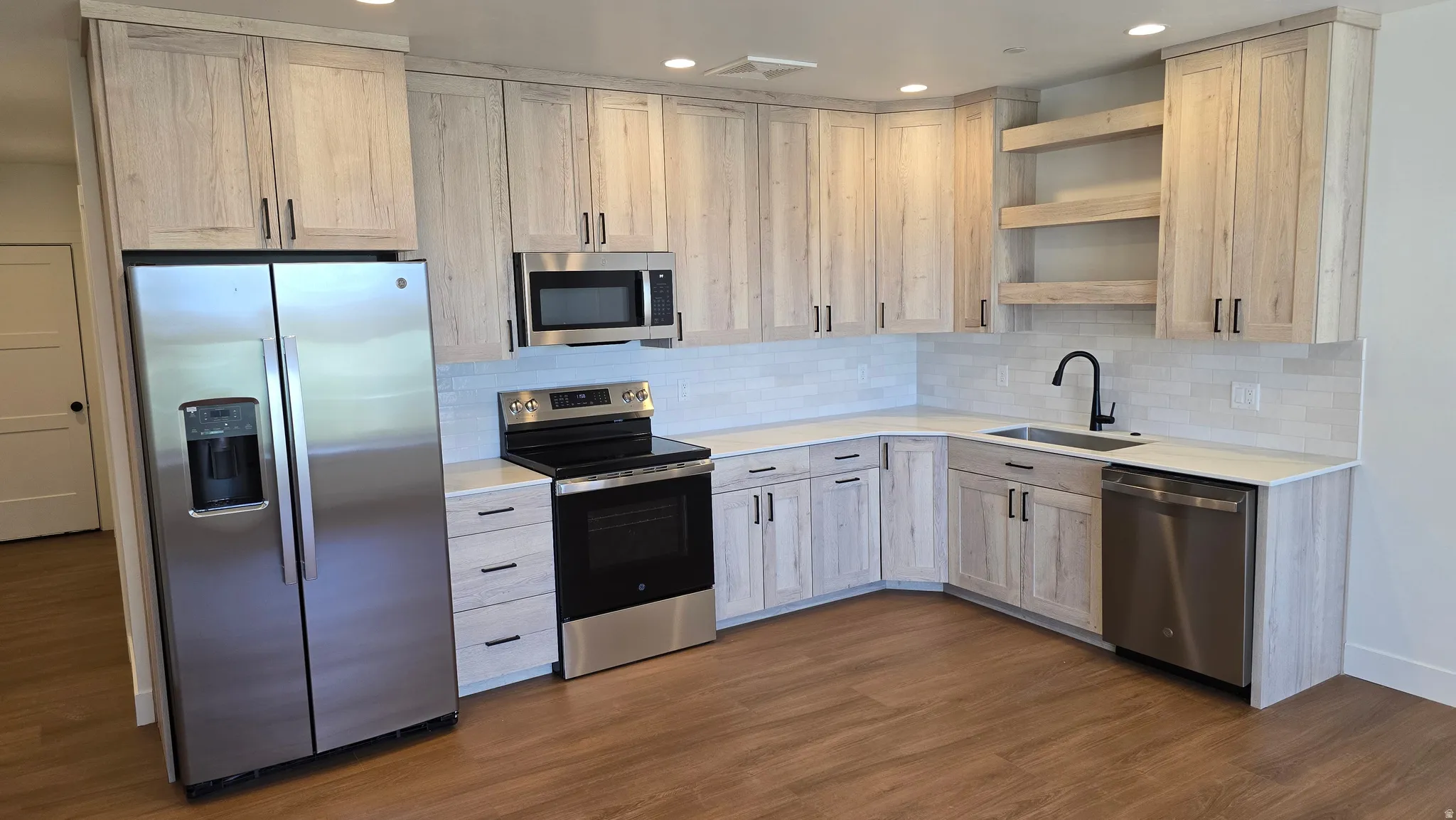 Kitchen featuring wood-finish flooring, light-toned cabinetry with matte black hardware, stainless steel appliances, white subway tile backsplash, and recessed lighting