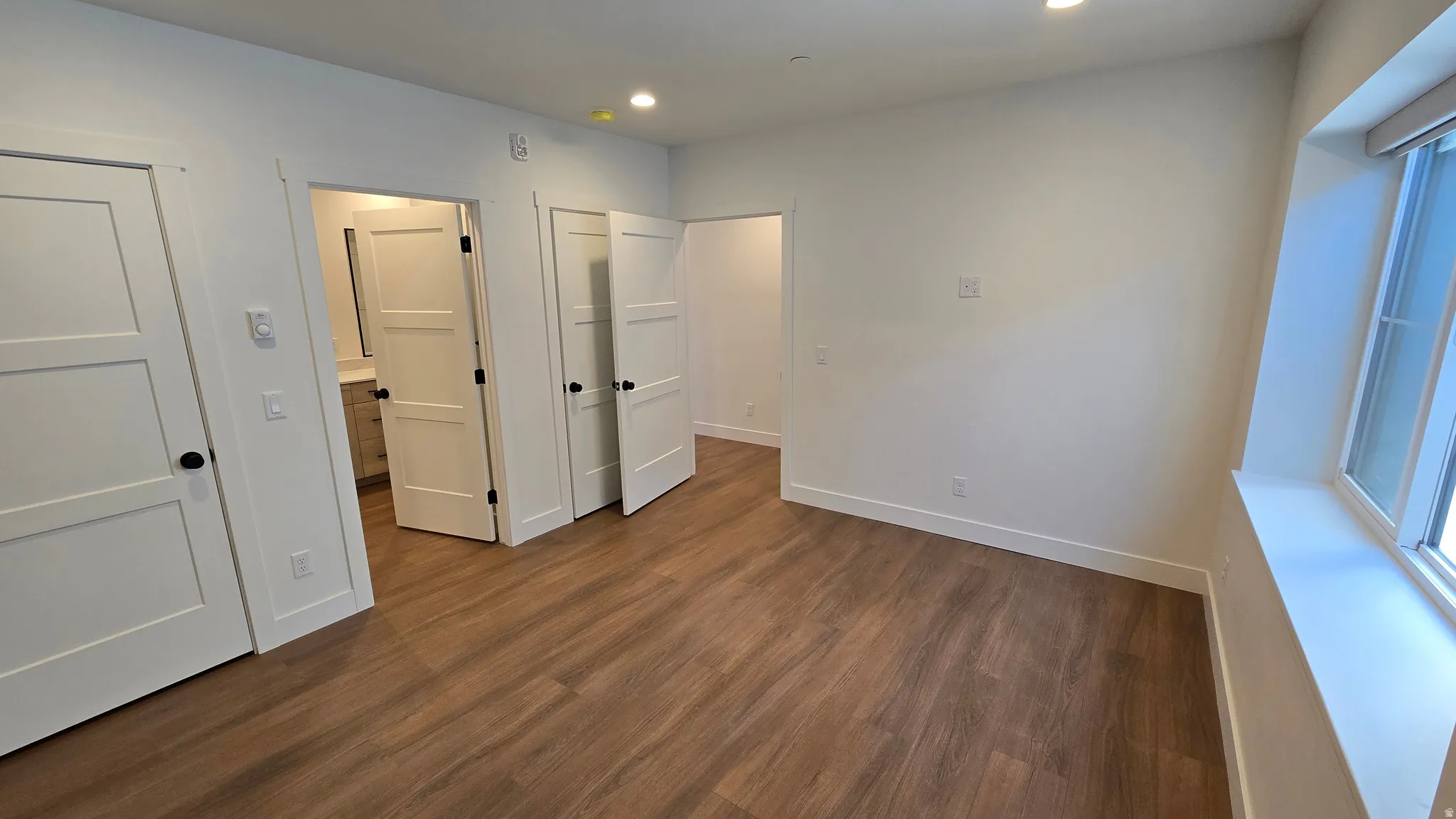 Spacious interior room featuring wood-finish flooring, white walls, and recessed lighting
