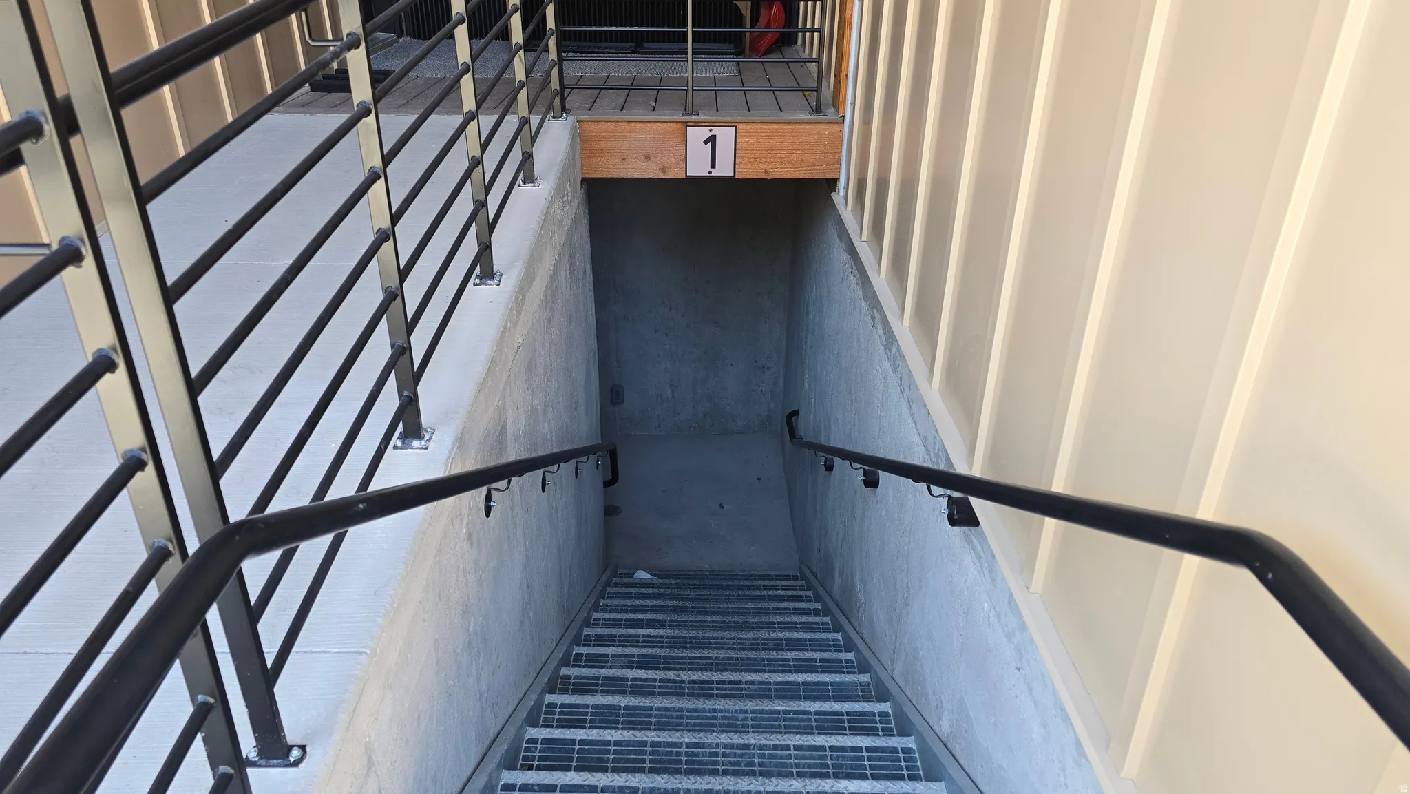 Concrete and metal staircase featuring sturdy black metal railings, a grated tread surface, and a numerical indicator