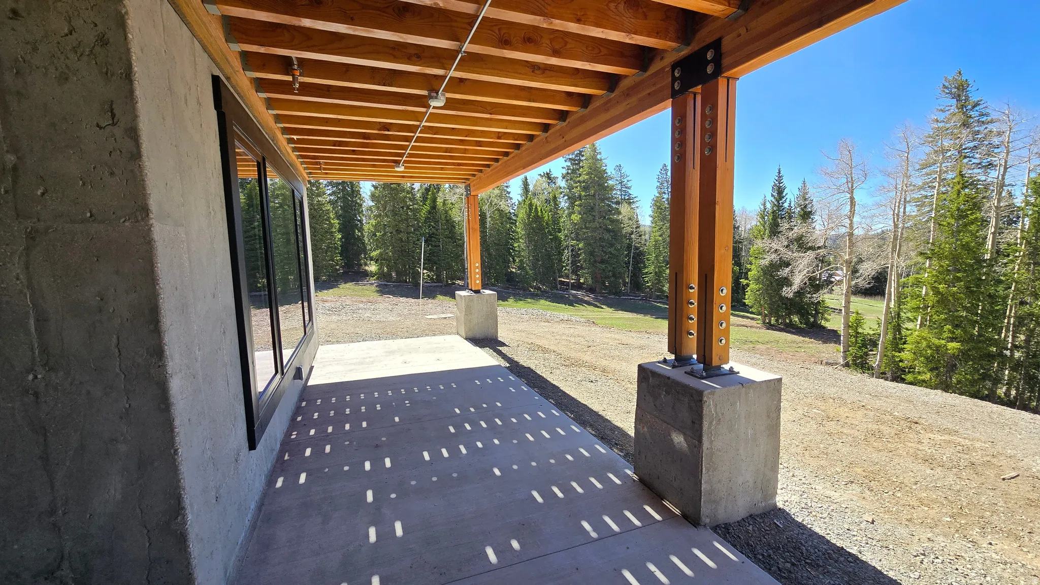 Covered concrete patio featuring exposed wood beams, concrete support columns, and large black-framed windows