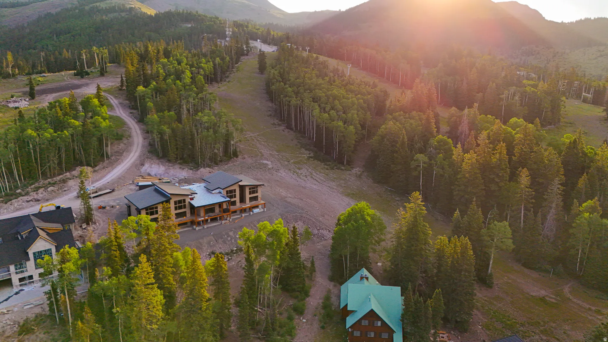 Mountainous terrain with a partially constructed multi-story residence featuring wood-finish siding, dark framed windows, and a dark roof