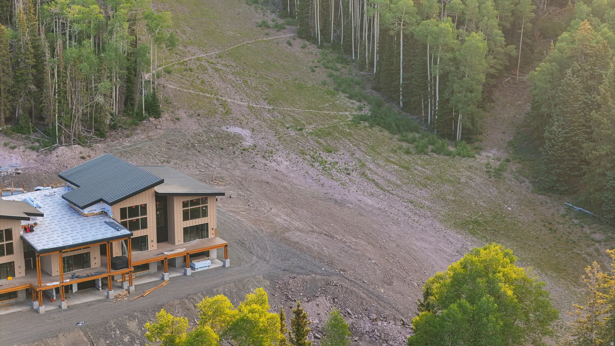 Expansive mountain-side property featuring a multi-level structure with a dark-pitched roof, numerous large windows, and a surrounding deck