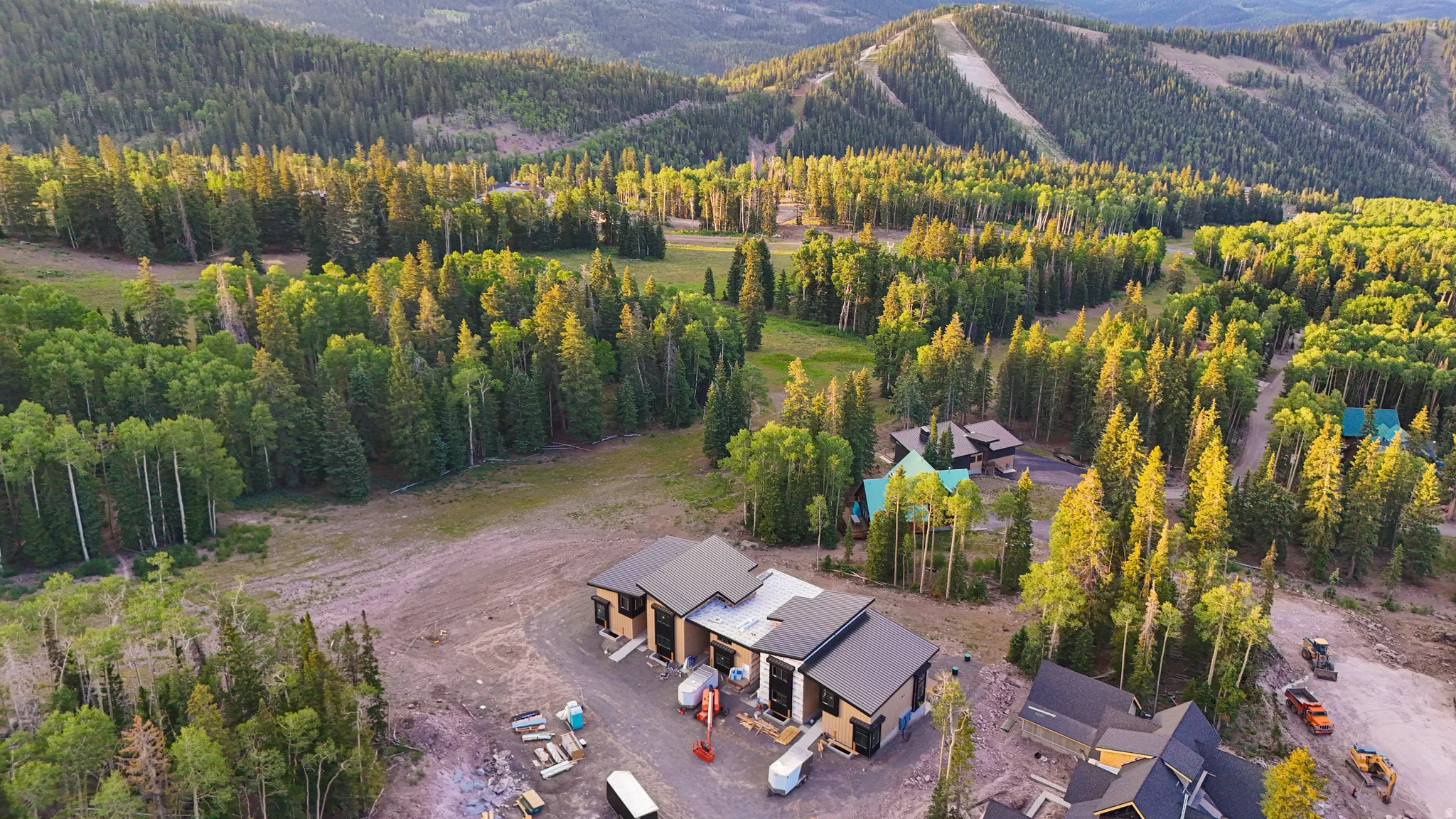 Contemporary mountain residence featuring a dark-toned roof and light-colored siding, situated amidst a dense forest of evergreen and deciduous trees