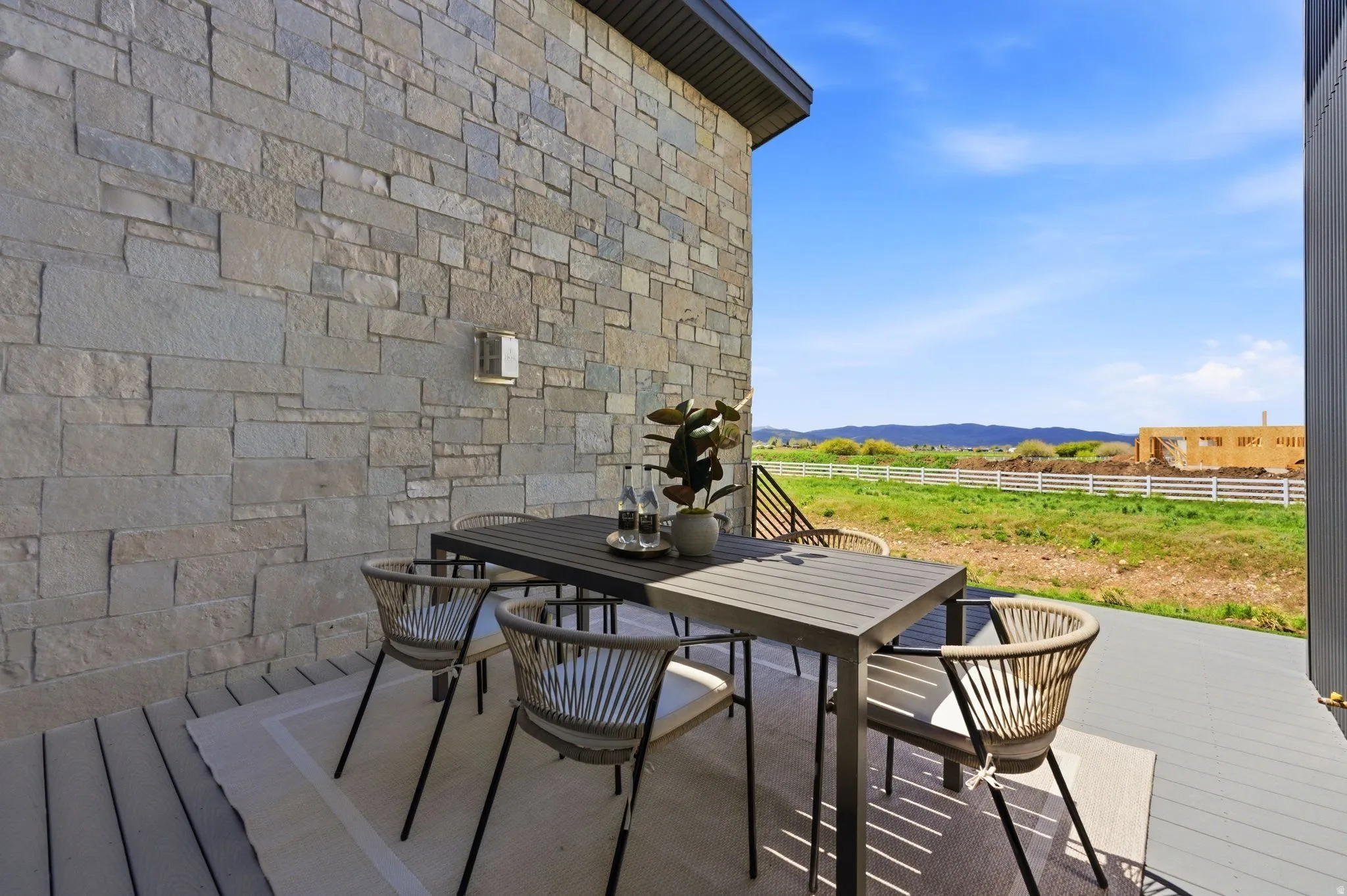 Outdoor patio featuring a stone-clad exterior wall with an attached sconce, composite decking, and a metal railing