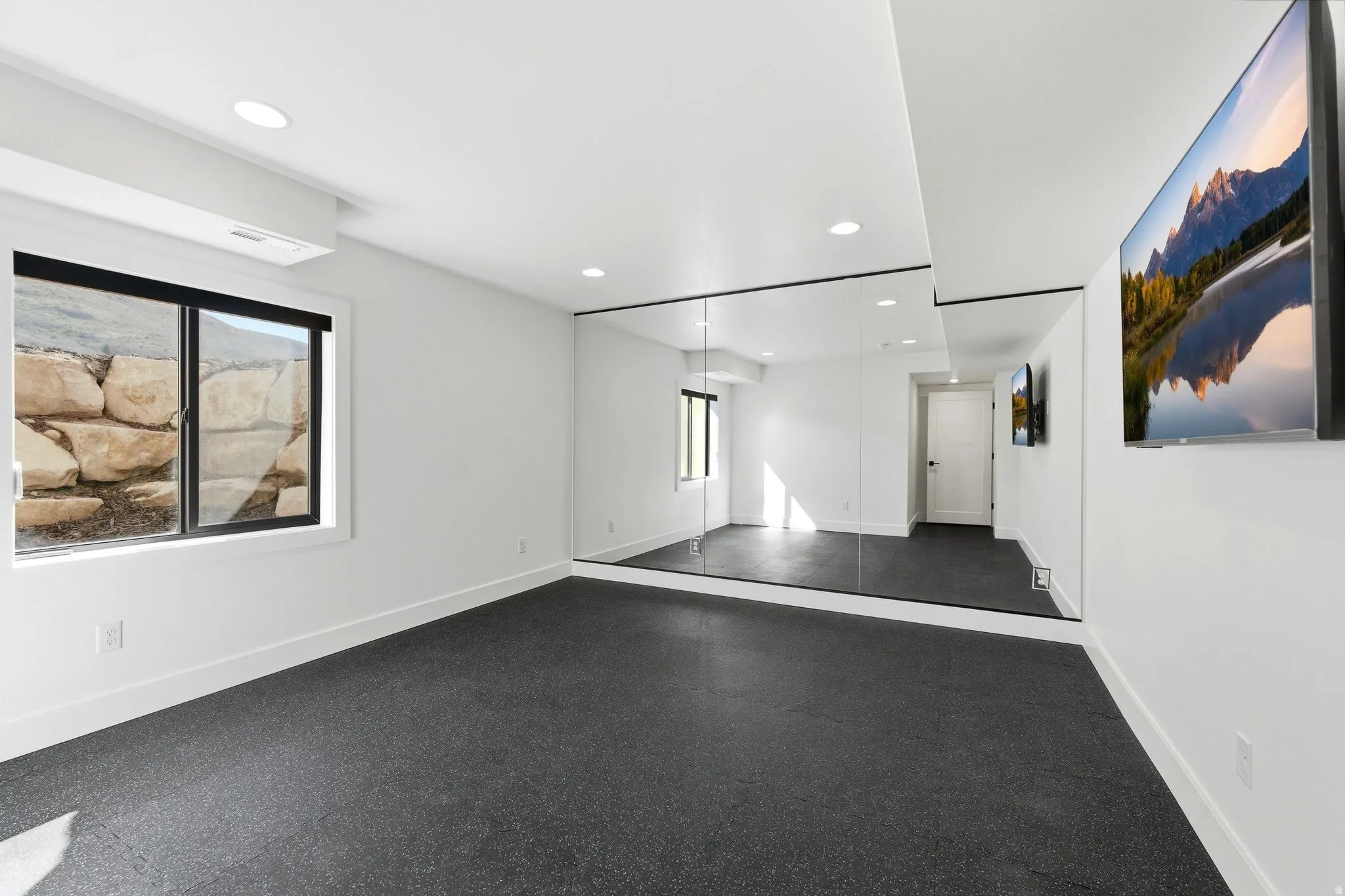 Versatile room featuring dark-toned resilient flooring, a full wall of mirrors, recessed lighting, and a single window
