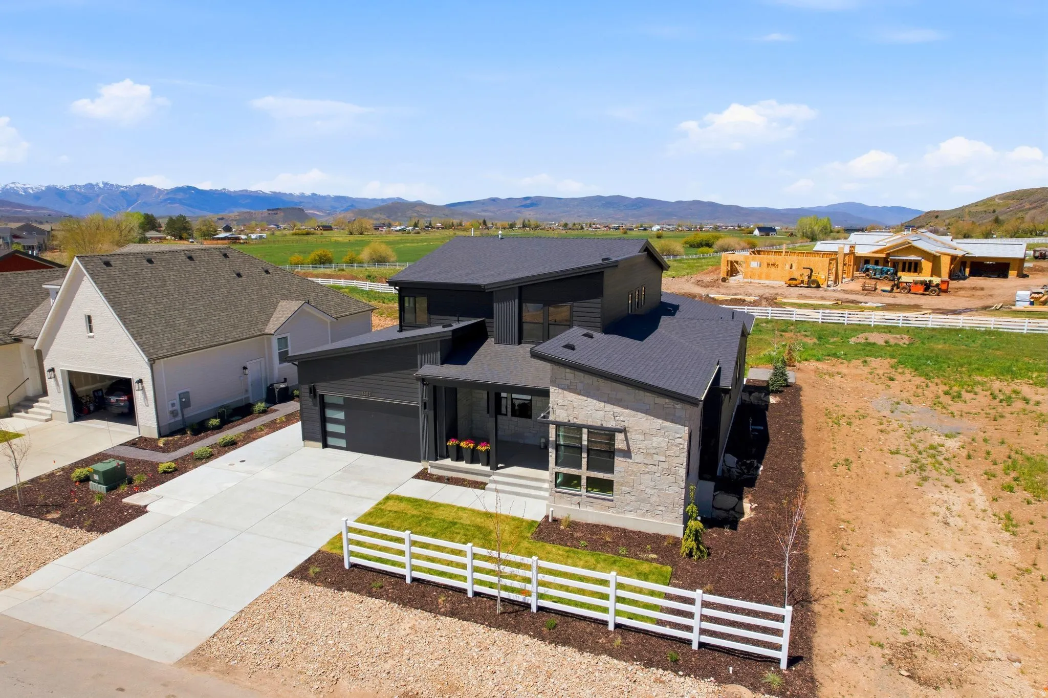 Contemporary multi-level residence featuring a dark siding exterior with stone accents, a multi-car driveway, and a white picket fence