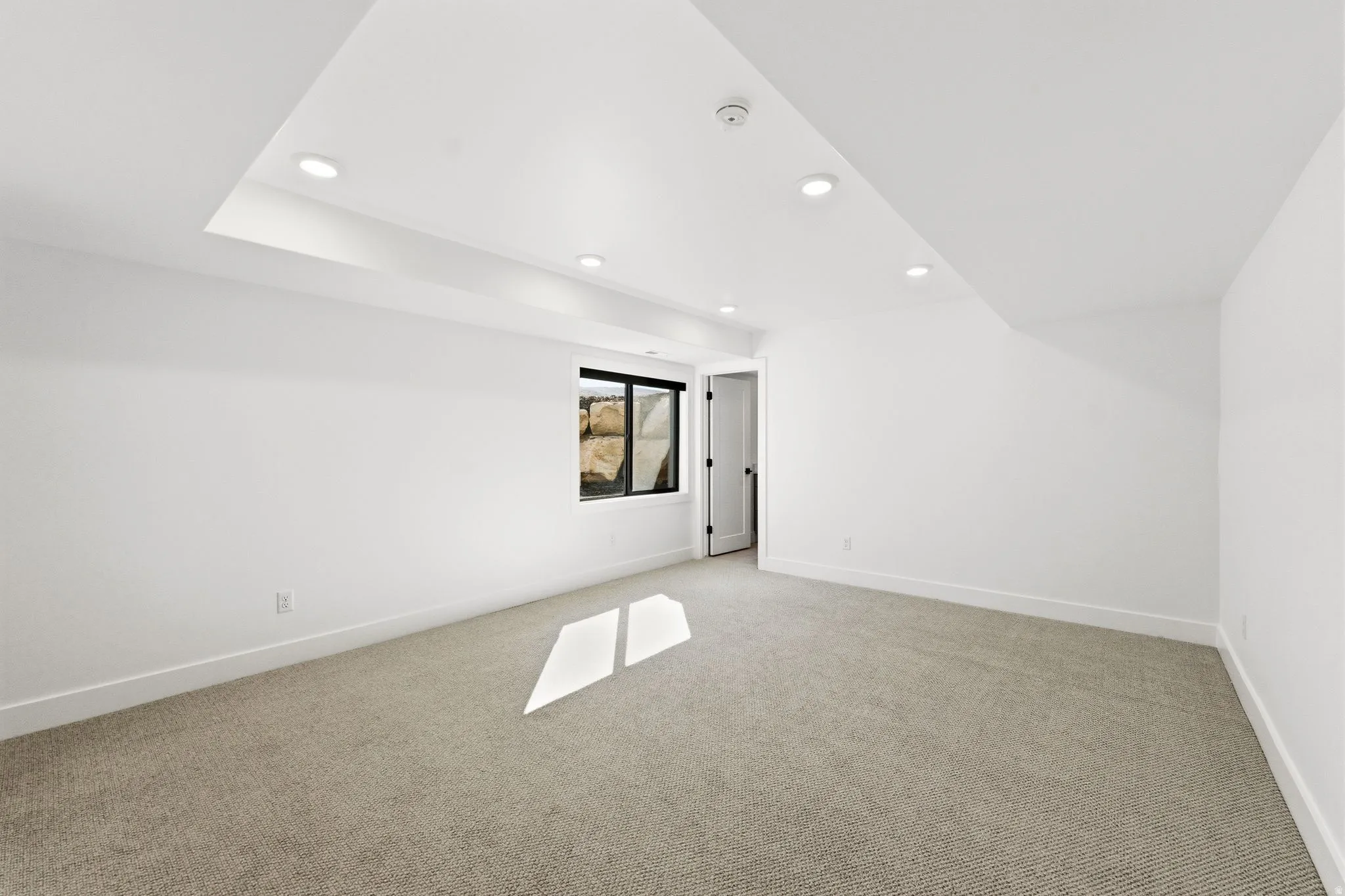 Carpeted room featuring recessed lighting, a white painted door, a window with black trim, and a tray ceiling
