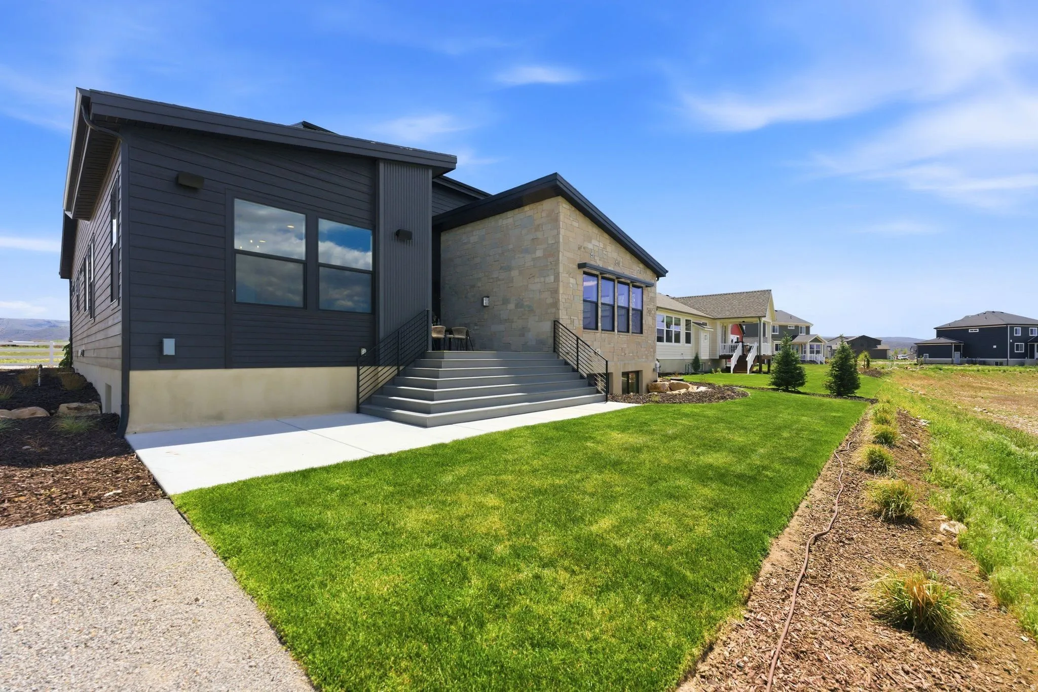 Contemporary exterior featuring dark horizontal siding, stone veneer accents, multi-pane windows, and a tiered concrete staircase with metal railings