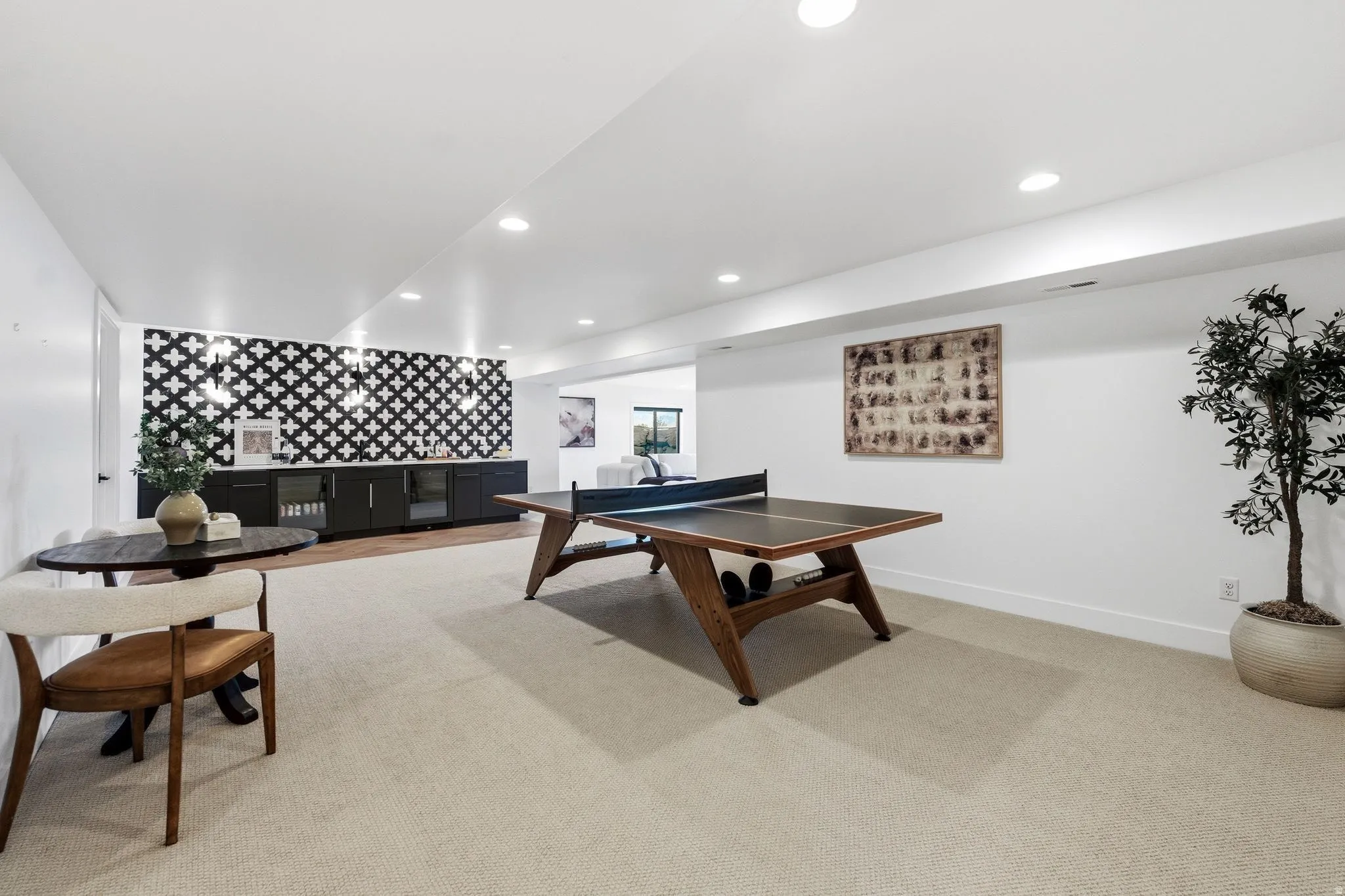 Expansive entertainment area featuring recessed lighting, light-toned carpeting, and a built-in wet bar with a distinctive tiled backsplash and integrated beverage refrigerators