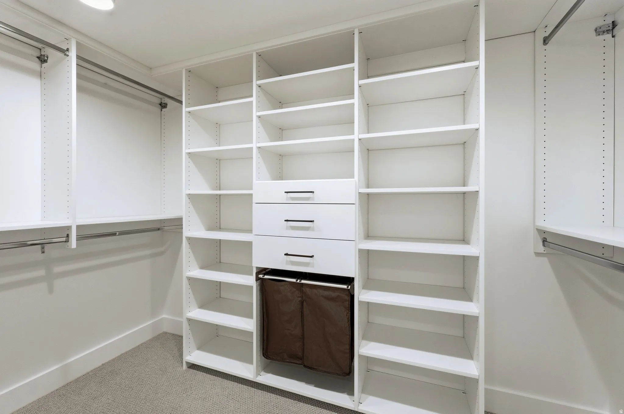 Custom closet system featuring white shelving, multiple hanging rods, three integrated drawers with dark hardware, and recessed ceiling lighting
