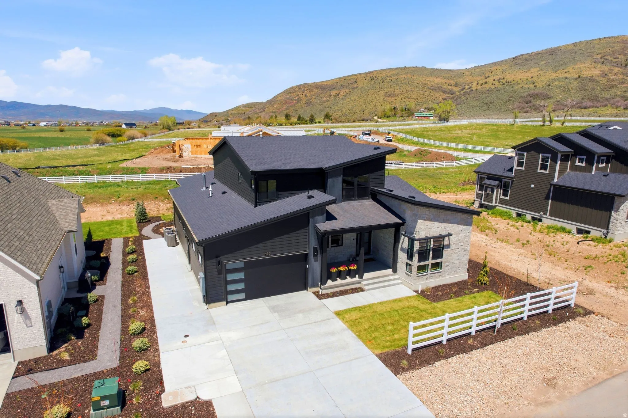 Modern architectural exterior featuring a dark facade, stone accents, a concrete driveway, and white picket fencing
