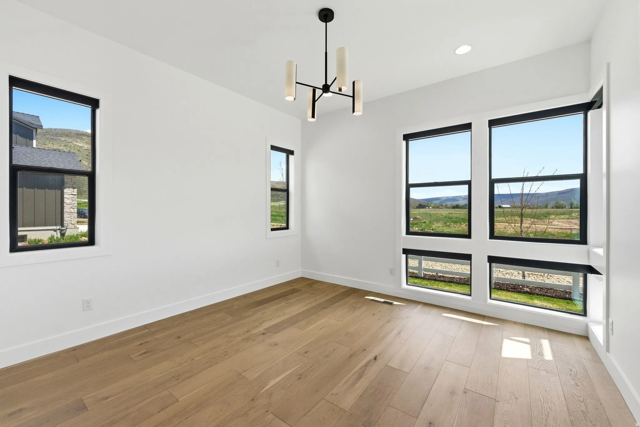 Expansive room featuring light wood-finish flooring, white walls, and a contemporary chandelier