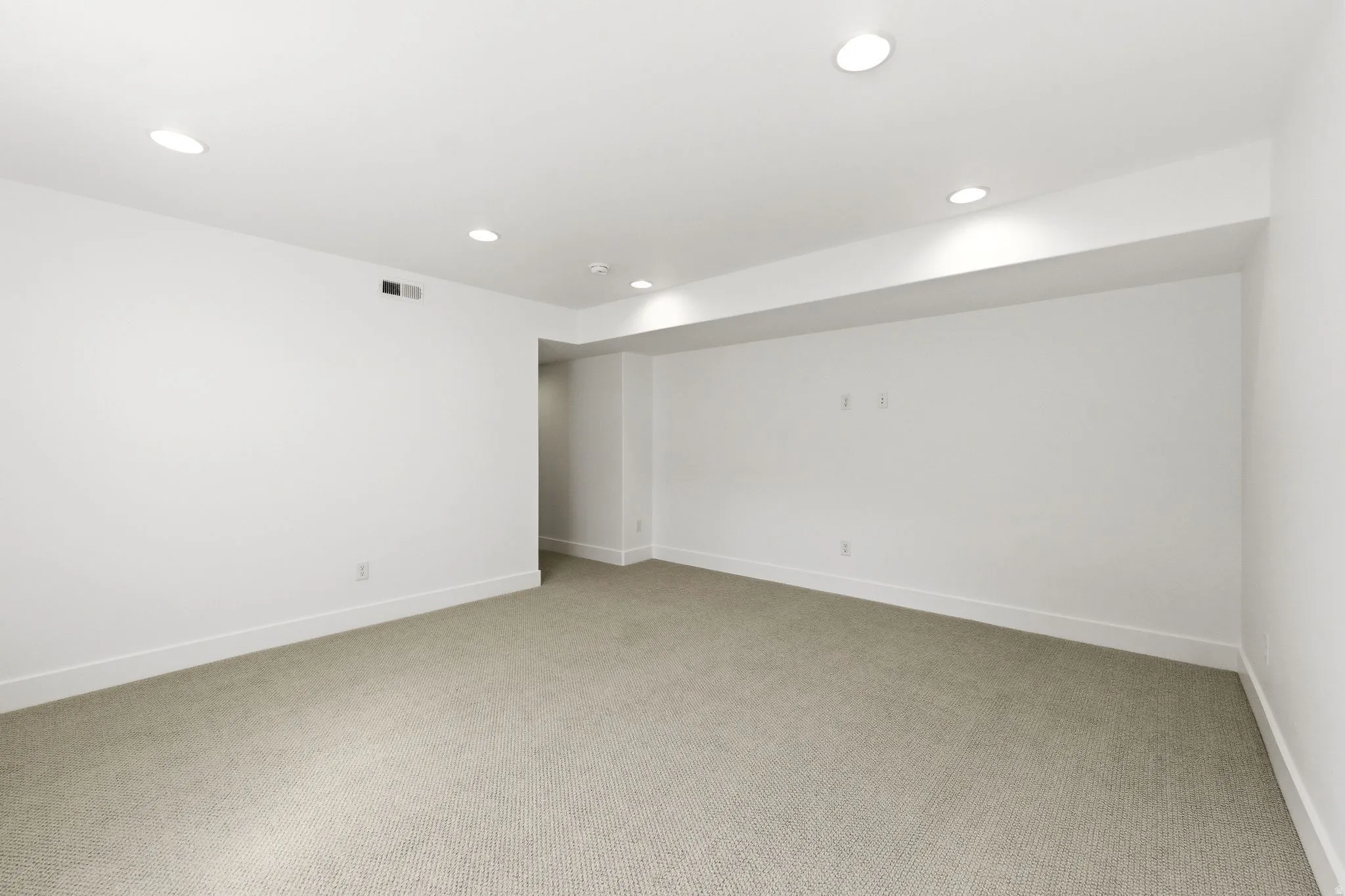 Spacious room featuring neutral carpeting, white walls, recessed lighting, white baseboards, and HVAC vents