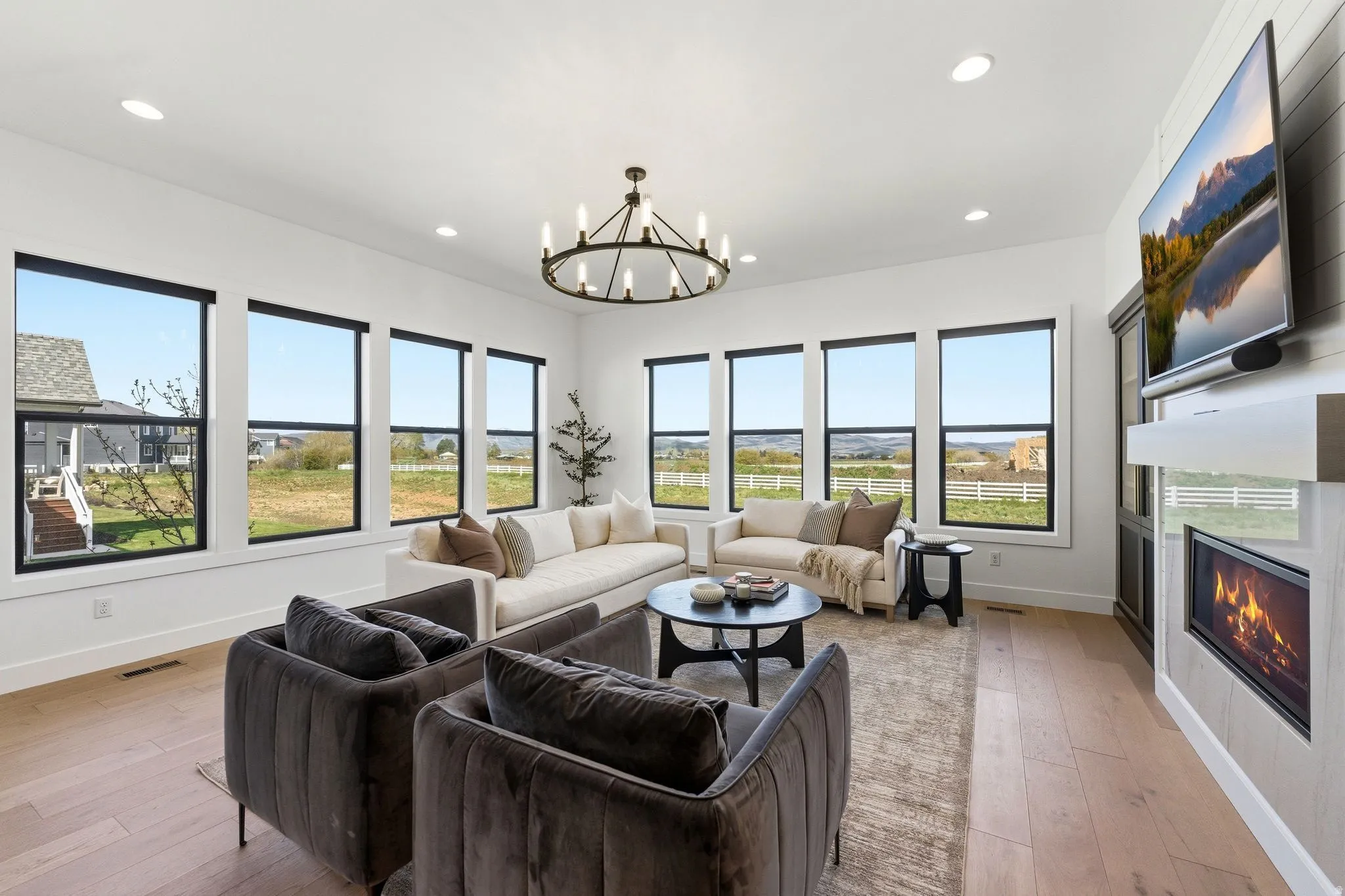 Expansive living area featuring multiple large windows, wood-finish flooring, a wall-mounted fireplace, a built-in entertainment center, and a contemporary chandelier
