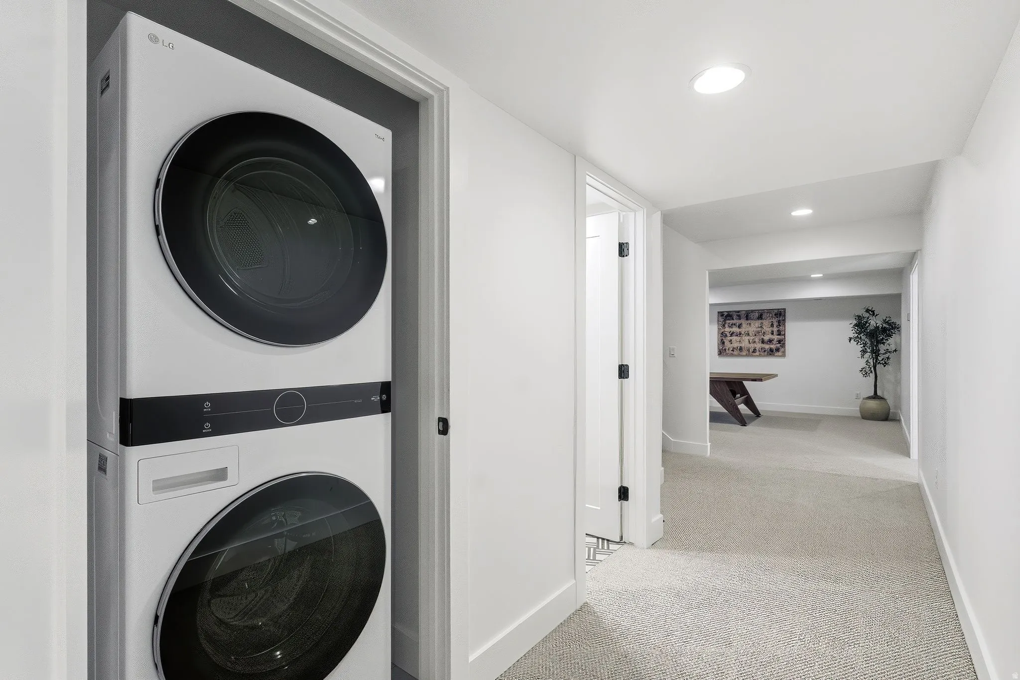 Integrated laundry closet featuring a stackable washer and dryer, recessed lighting, white walls, and light-toned carpet flooring throughout the hallway
