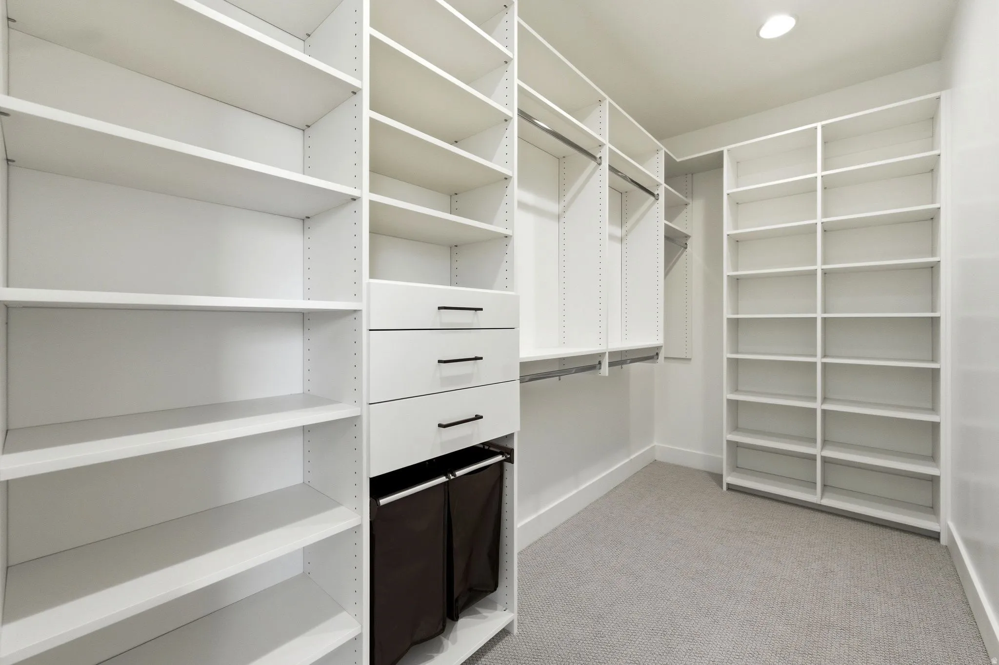 Custom closet system featuring extensive shelving, multiple hanging rods, built-in drawers with modern pulls, recessed lighting, and soft carpet flooring