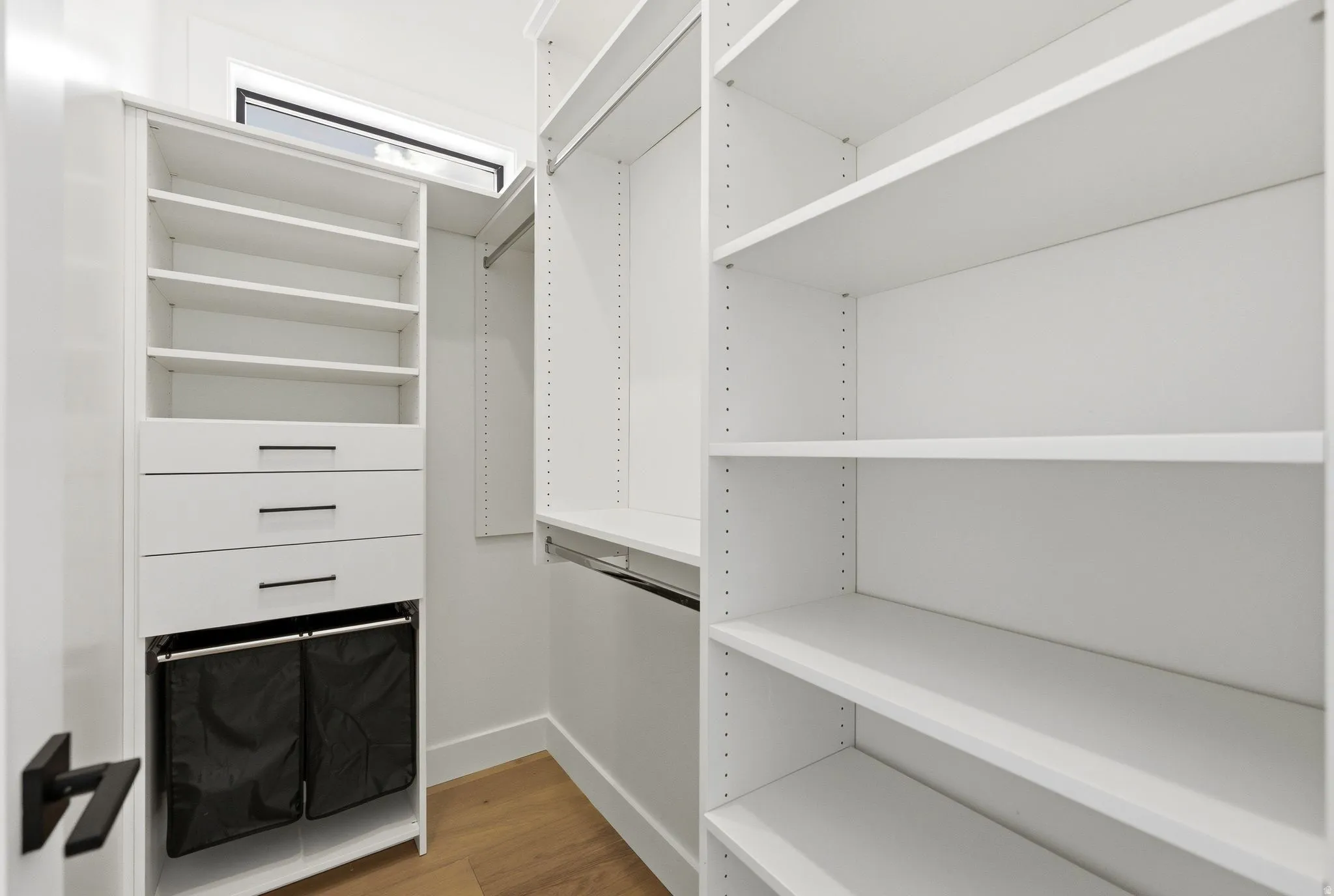 Custom closet system featuring white shelving, integrated drawers with linear hardware, and wood-finish flooring