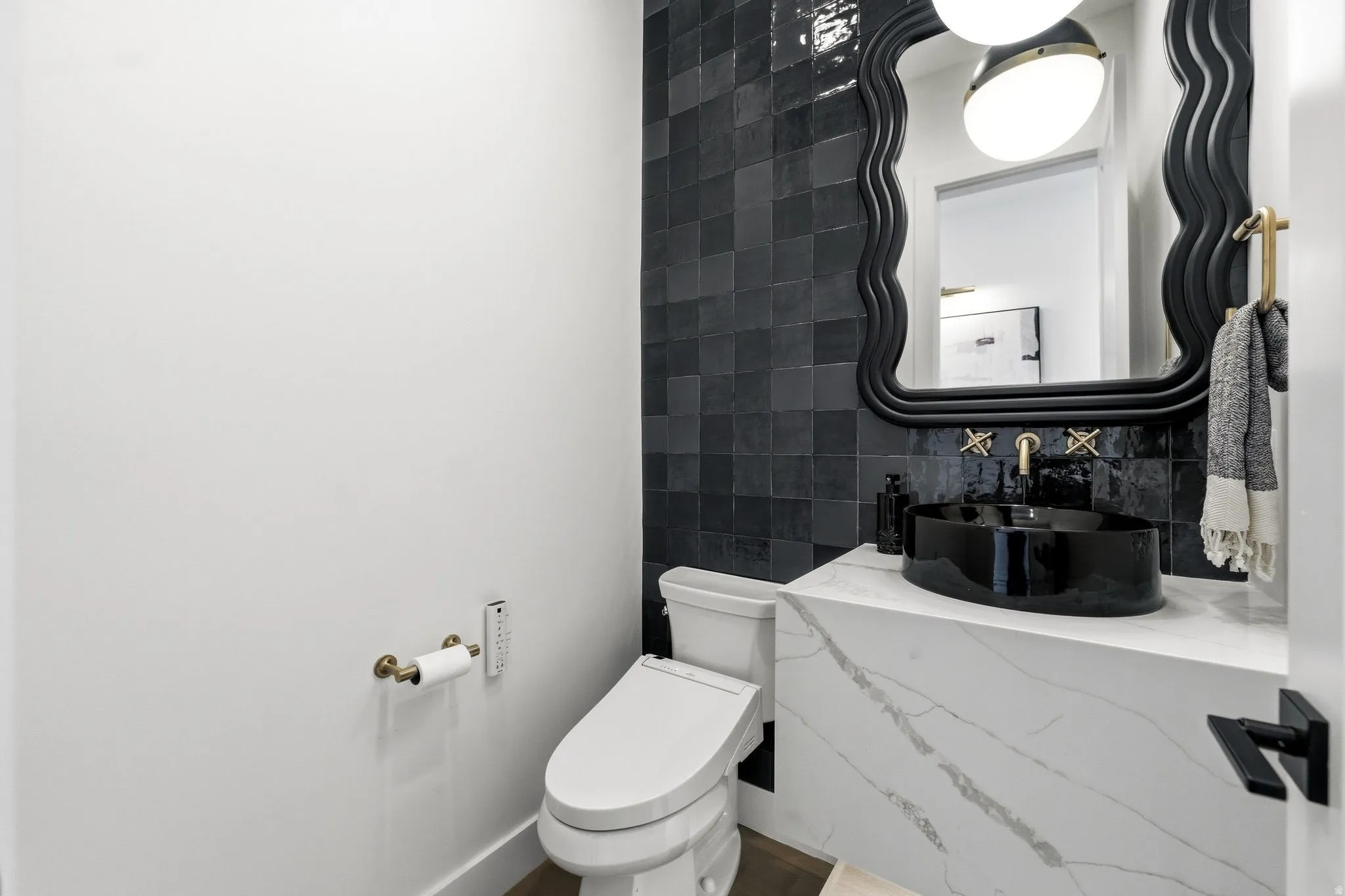 Modern powder room featuring a black vessel sink, gold-finish wall-mounted faucet, and a sleek, white toilet
