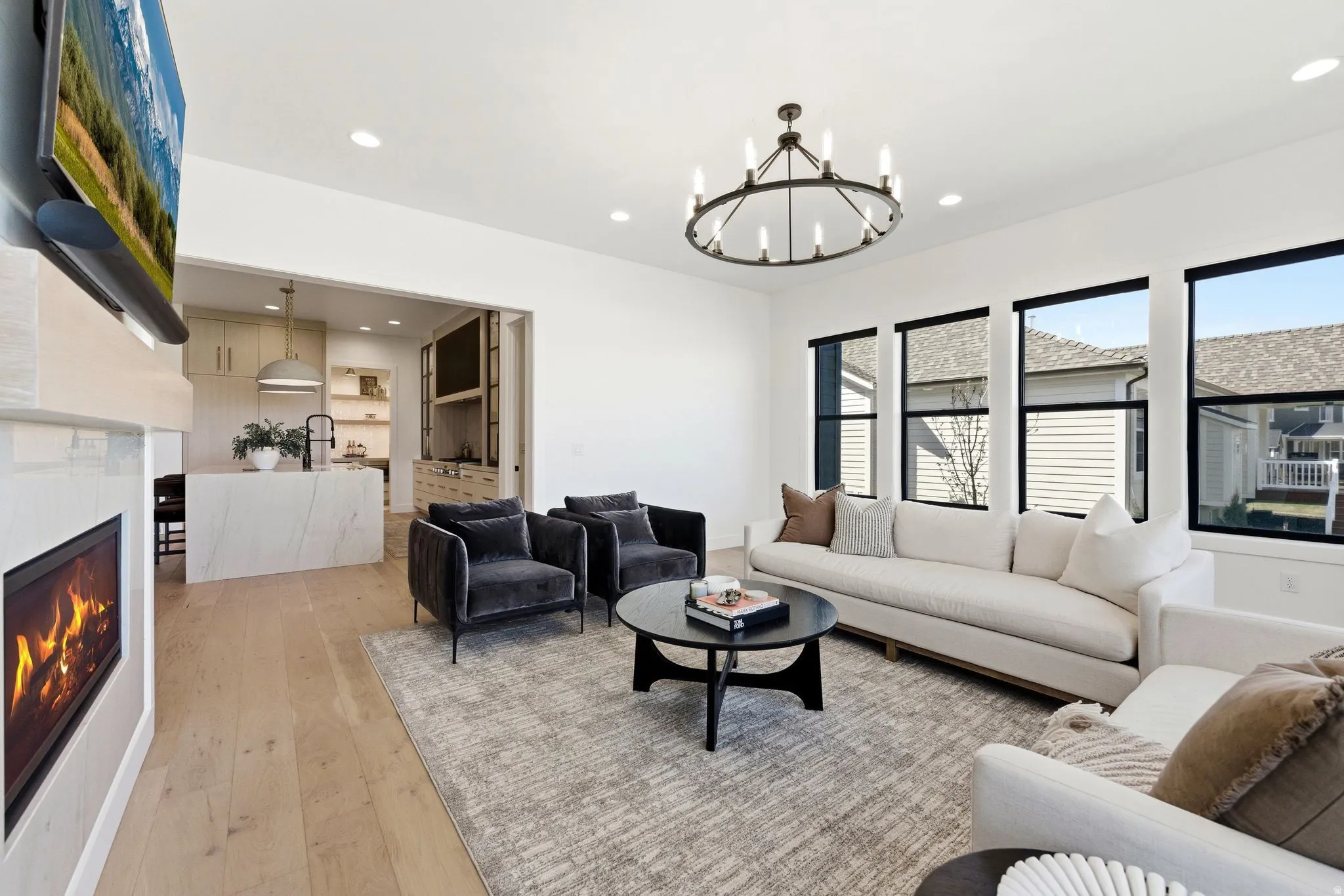 Spacious living area featuring light wood-finish flooring, a contemporary fireplace with a stone surround, and recessed lighting