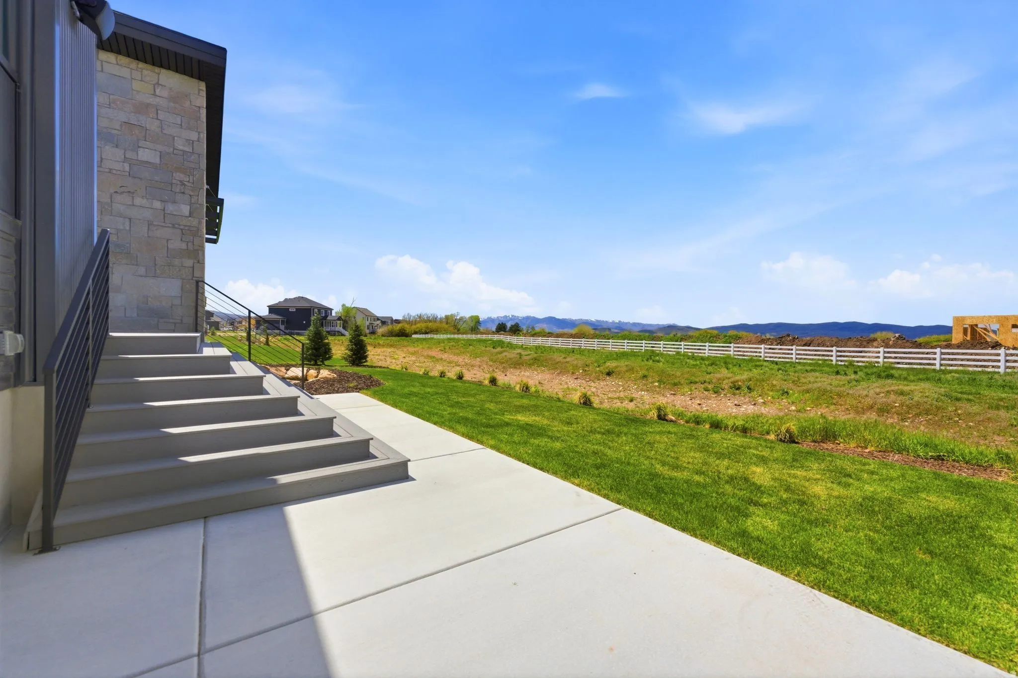 Stairway access to the property featuring stone-clad exterior, black metal handrails, a concrete path, and expansive green space