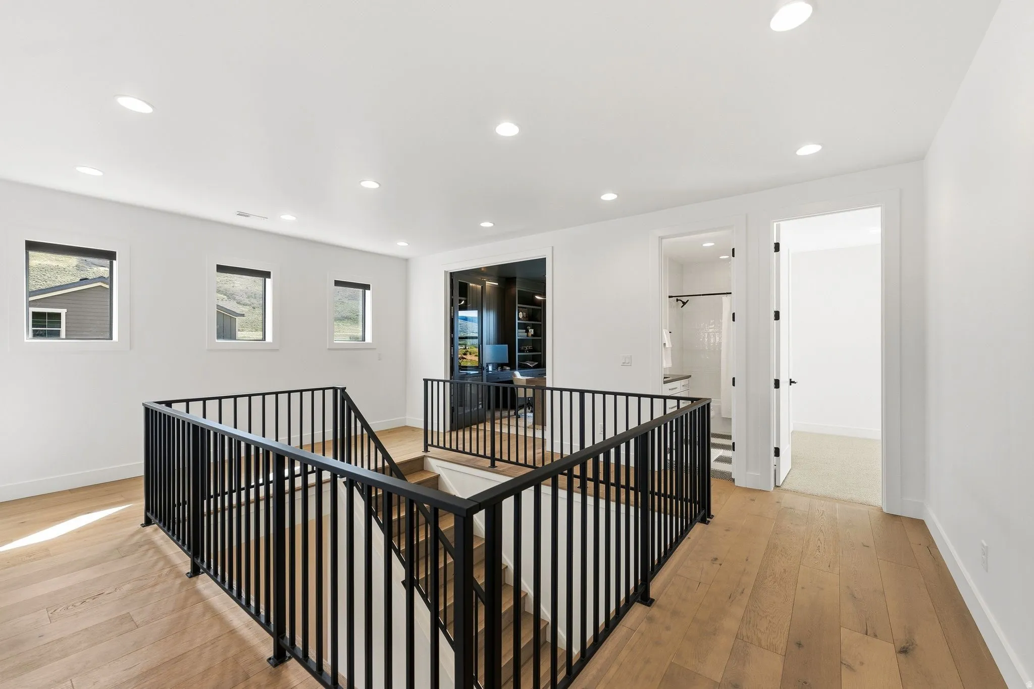Upper-level landing featuring wood-finish flooring, recessed lighting, black metal railings, and multiple windows