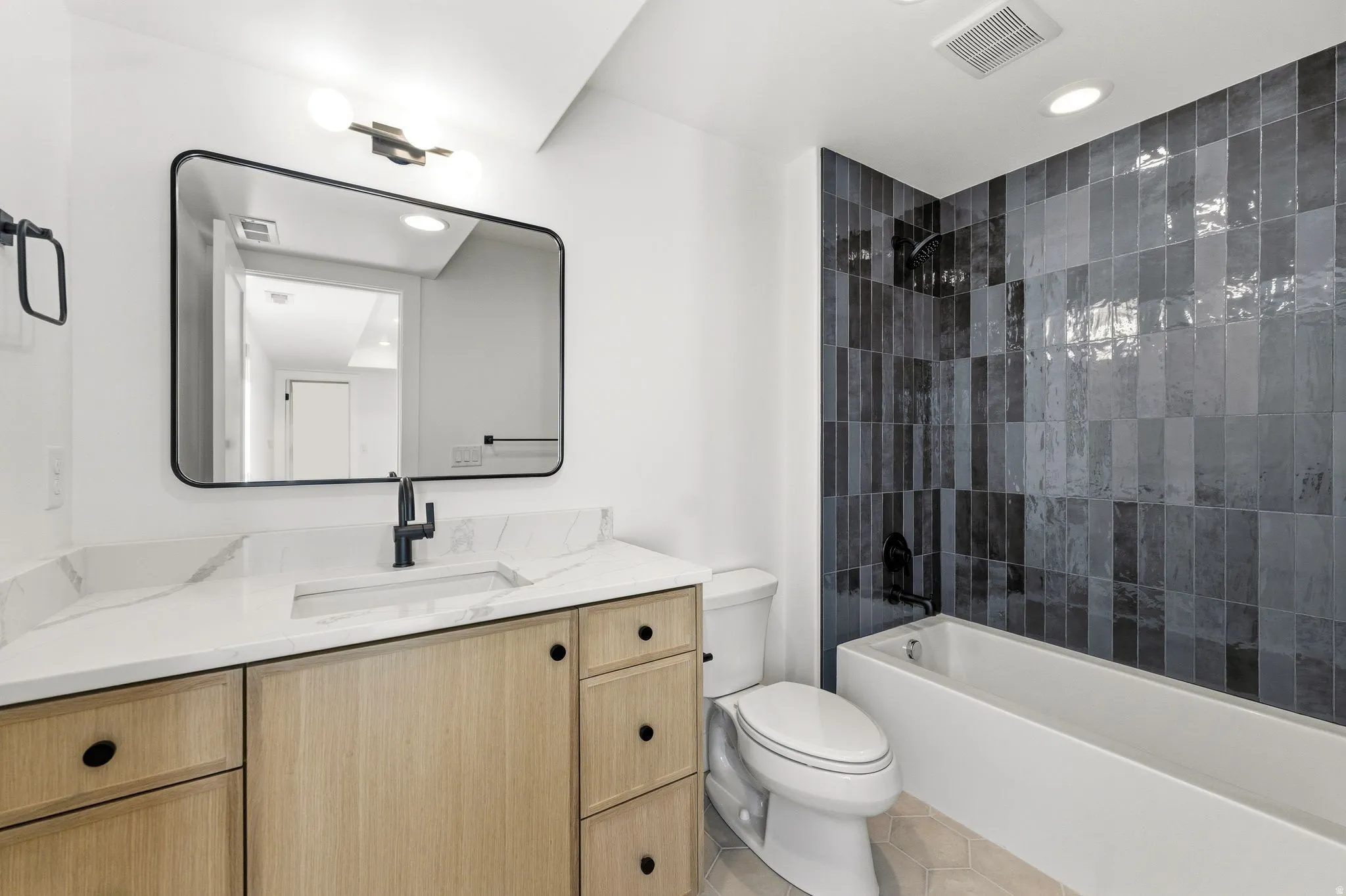 Bathroom featuring a light wood-finish vanity with a white countertop and integrated sink, a black-framed rectangular mirror, and matte black fixtures