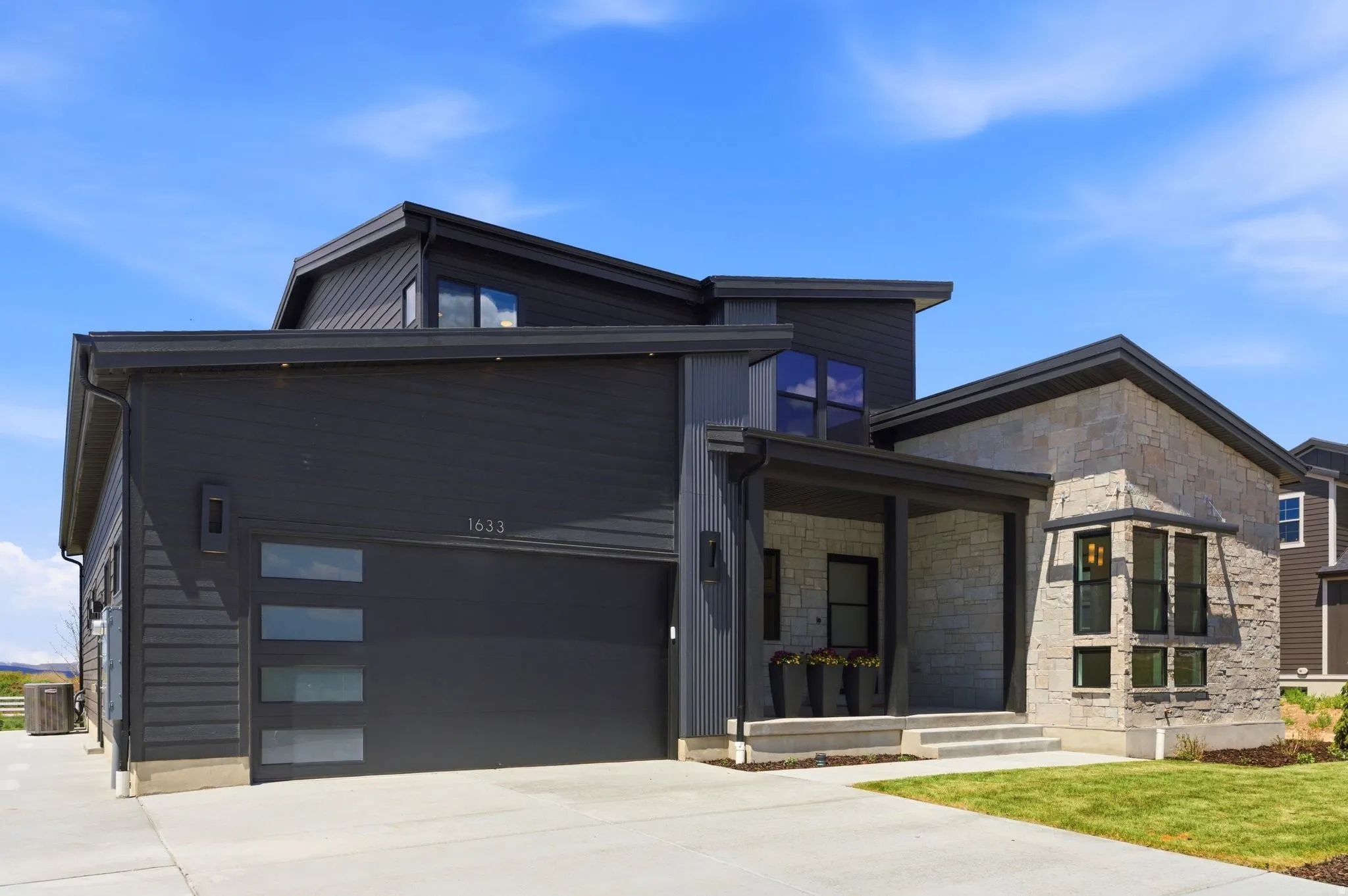 Contemporary exterior featuring dark horizontal siding, natural stone accents, a covered entry, and an integrated garage with frosted glass panels