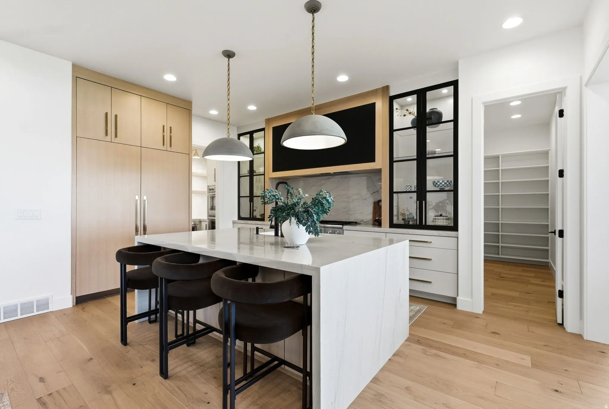 Gourmet kitchen featuring a substantial island with seating, pendant lighting, integrated wood-finish appliances, light wood-finish flooring, and a walk-in pantry with extensive shelving